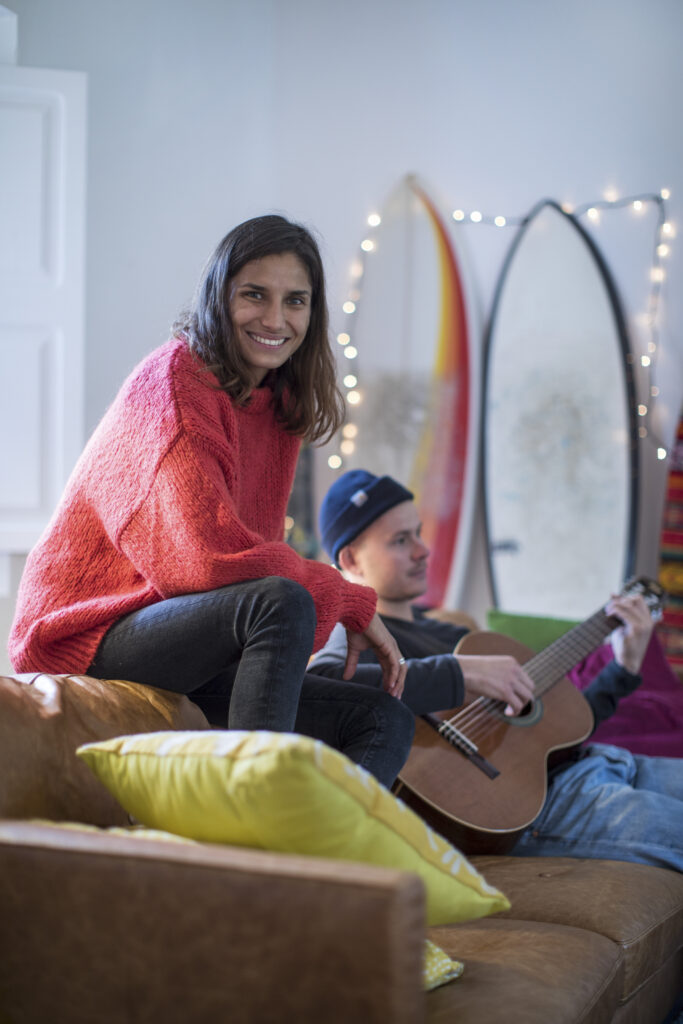 Young woman sitting up on living room sofa with young man playing guitar during a partial hospitalization program